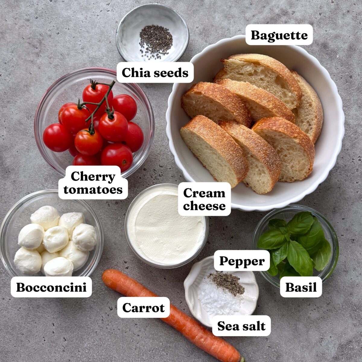 Cherry tomatoes, chia seeds, baguette slices, bocconcini, cream cheese, a carrot, pepper, sea salt, and fresh basil.