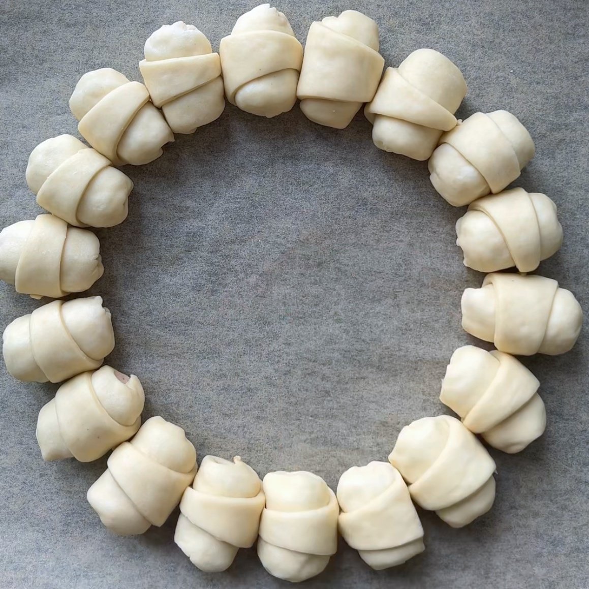 Unbaked sausage rolls arranged in a circle on parchment paper.