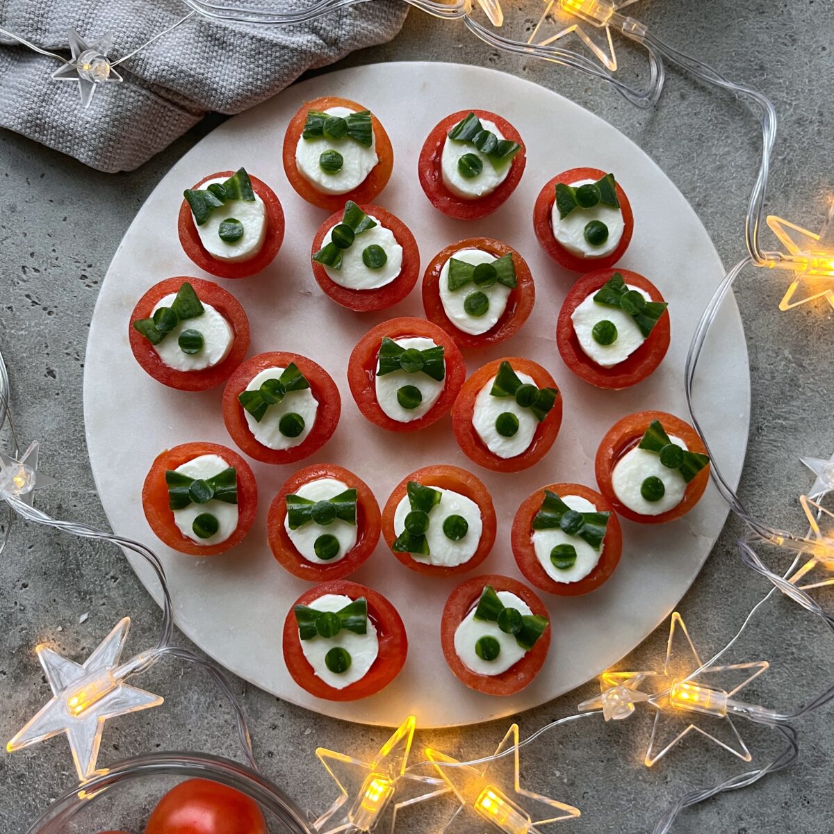 A round platter with cherry tomato appetizers stuffed and topped with mozzarella and cucumber, surrounded by star-shaped string lights.