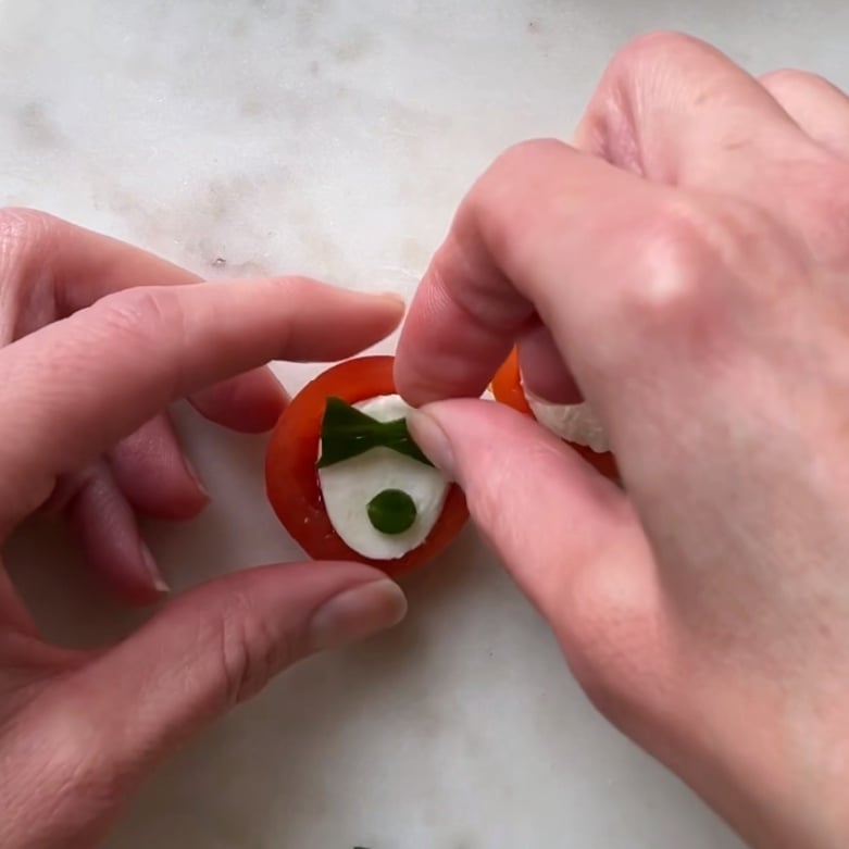 A hand places a cucumber butterfly and button detail on top of cherry tomato appetizers.