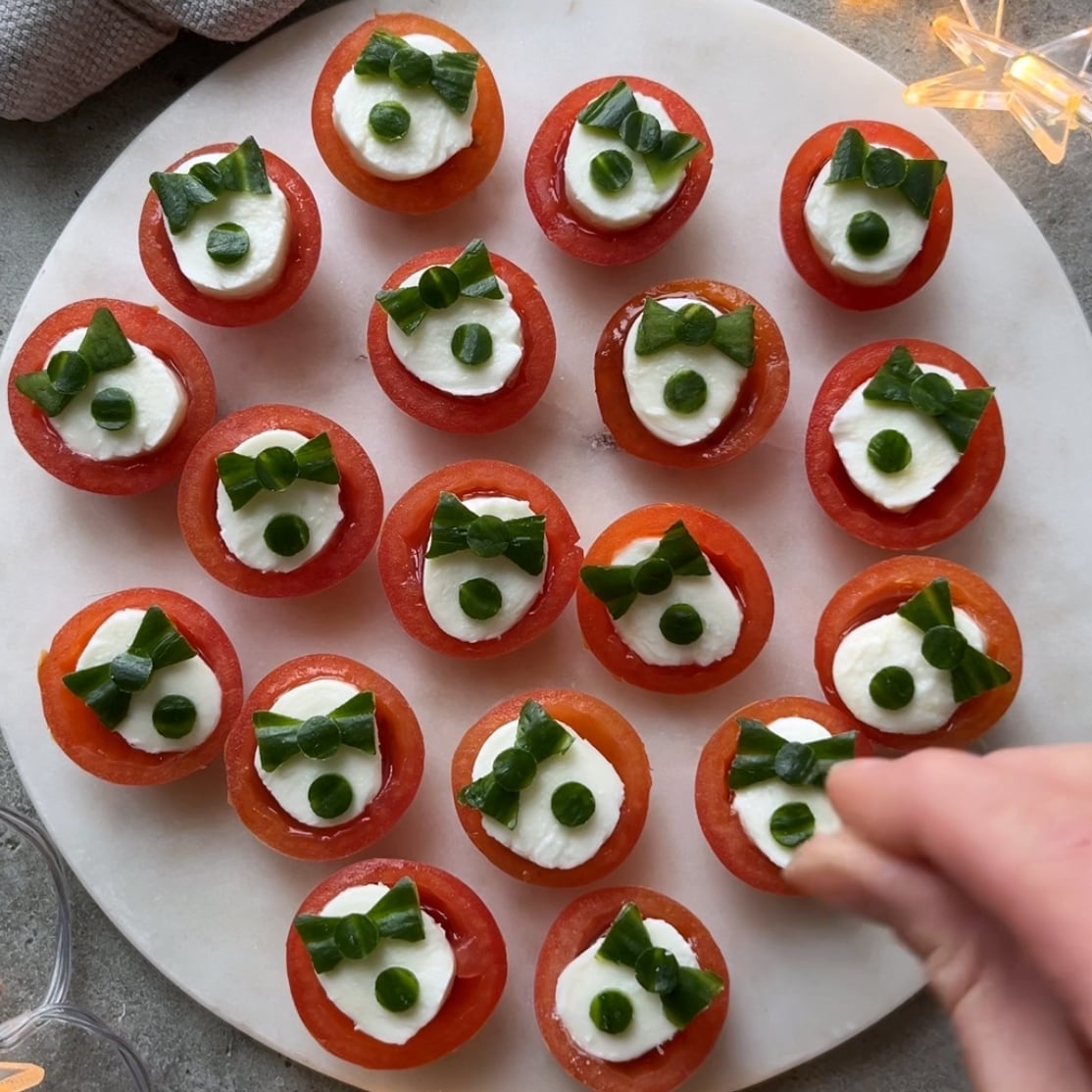A hand sprinkles sea salt on top of cherry tomato appetizers arranged on a white marble platter.