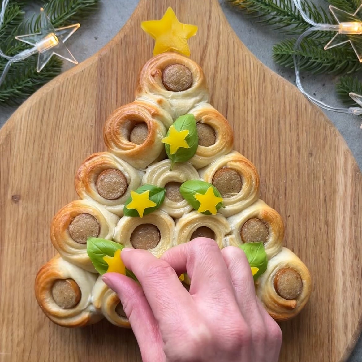 A hand places a yellow pepper star to garnish a baked pastry Christmas tree centerpiece.