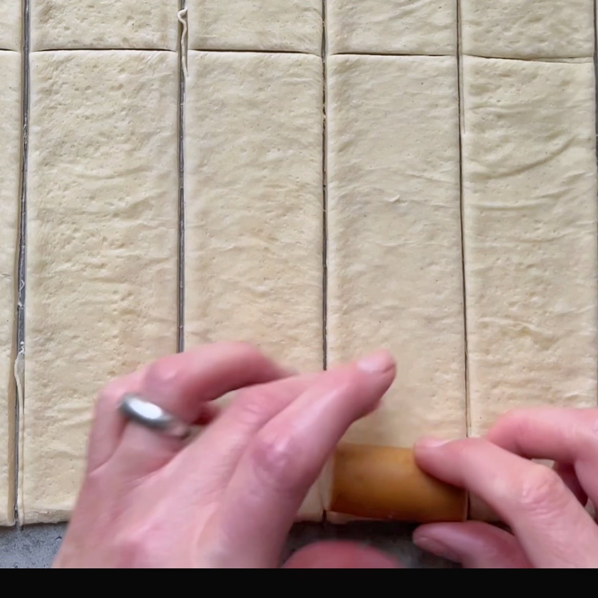 A piece of sausage is being placed at the base of a rectangular piece of pizza dough.