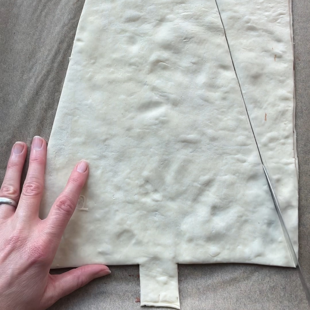 A hand cuts rolled pastry dough into a Nutella Christmas Tree shape with a knife on parchment paper.