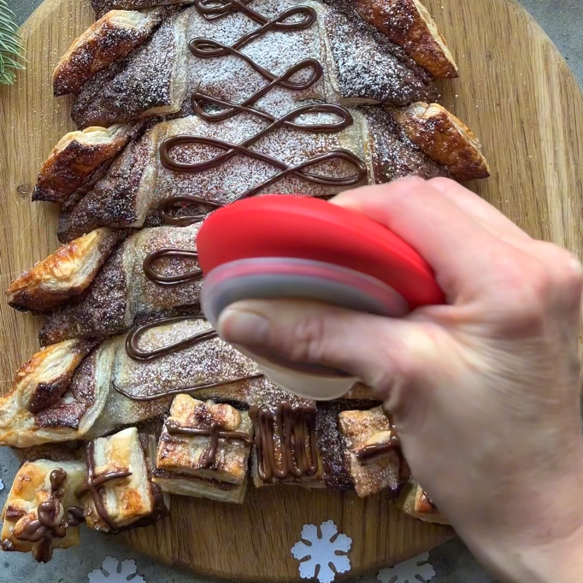A hand holds a red piping tool over a Nutella Christmas Tree puff pastry and tops it with chocolate swirl.