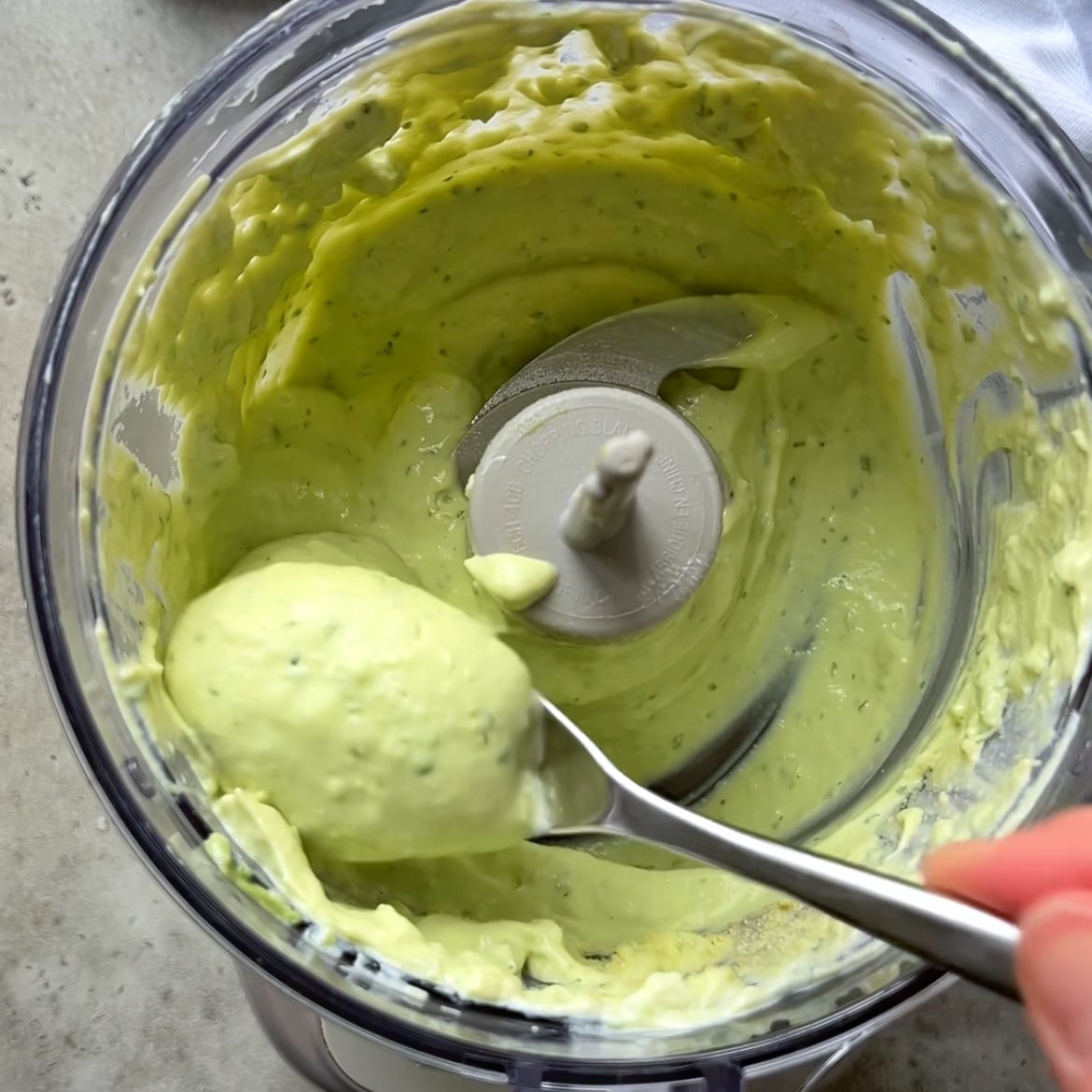 A spoon dips into a light green avocado cream made in a mini food processor.
