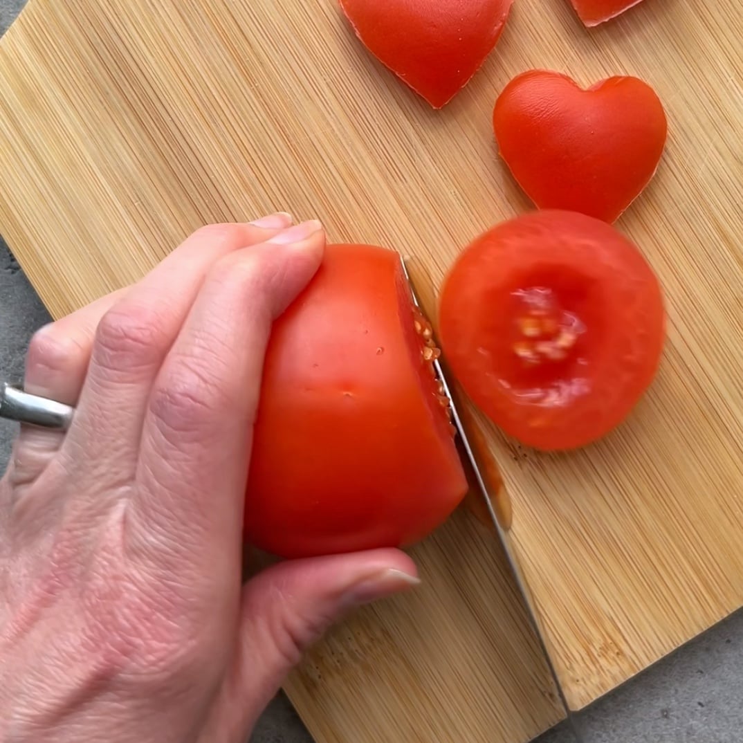A knife slices into a vine tomato, ready to cut out hearts.