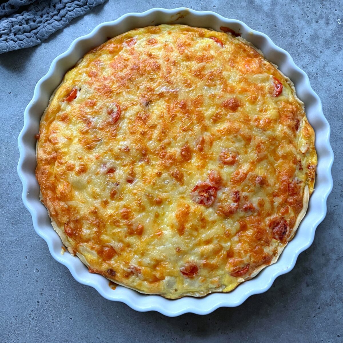 A baked Chicken Quiche with a golden-brown cheese topping in a white fluted ceramic dish.