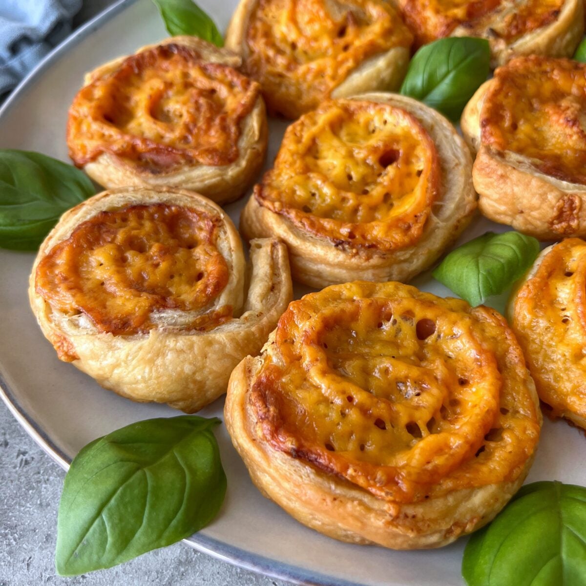 A plate of Ham and Cheese Pinwheels arranged with fresh basil leaves.