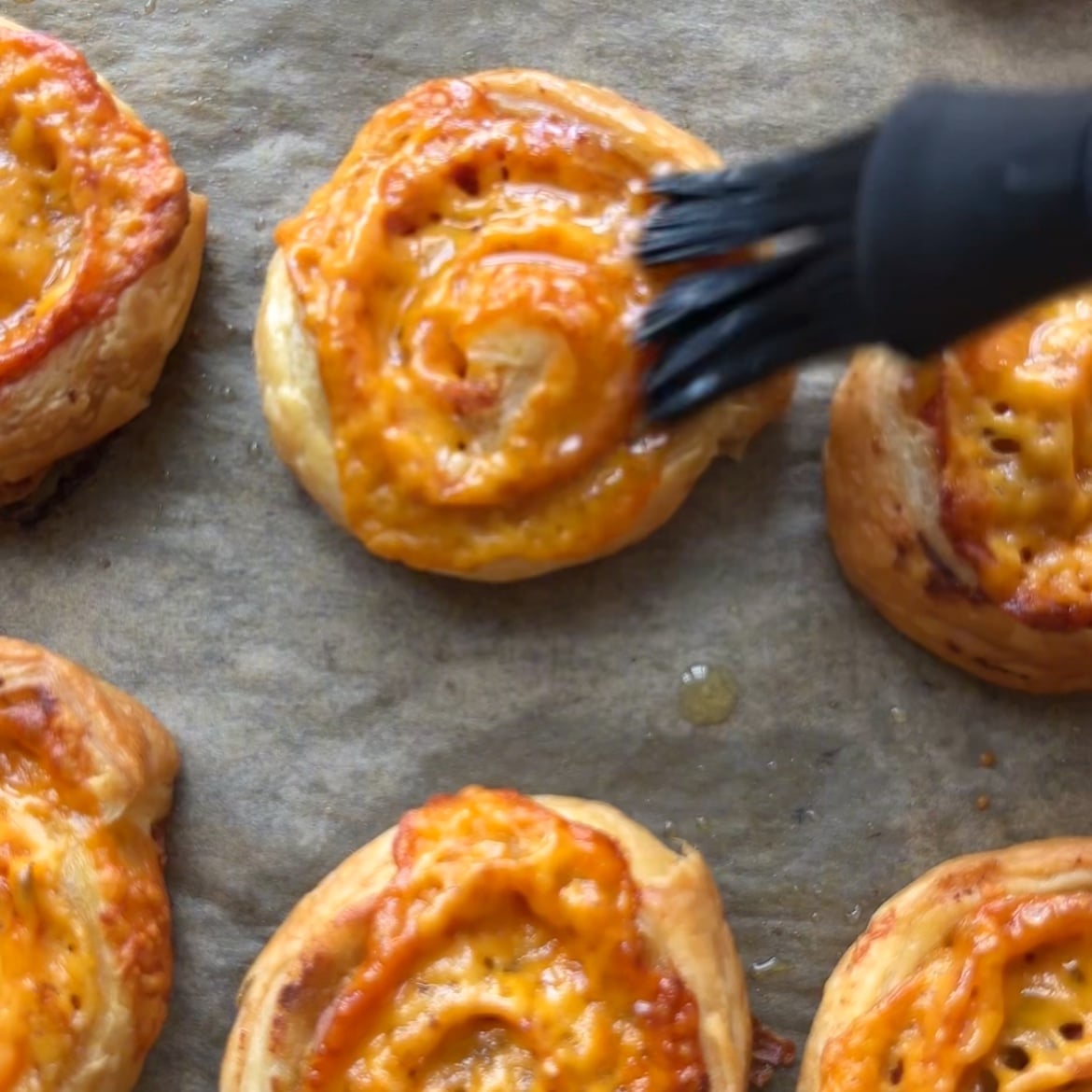 A pastry brush is being used to glaze freshly baked Ham and Cheese Pinwheels with garlic butter.