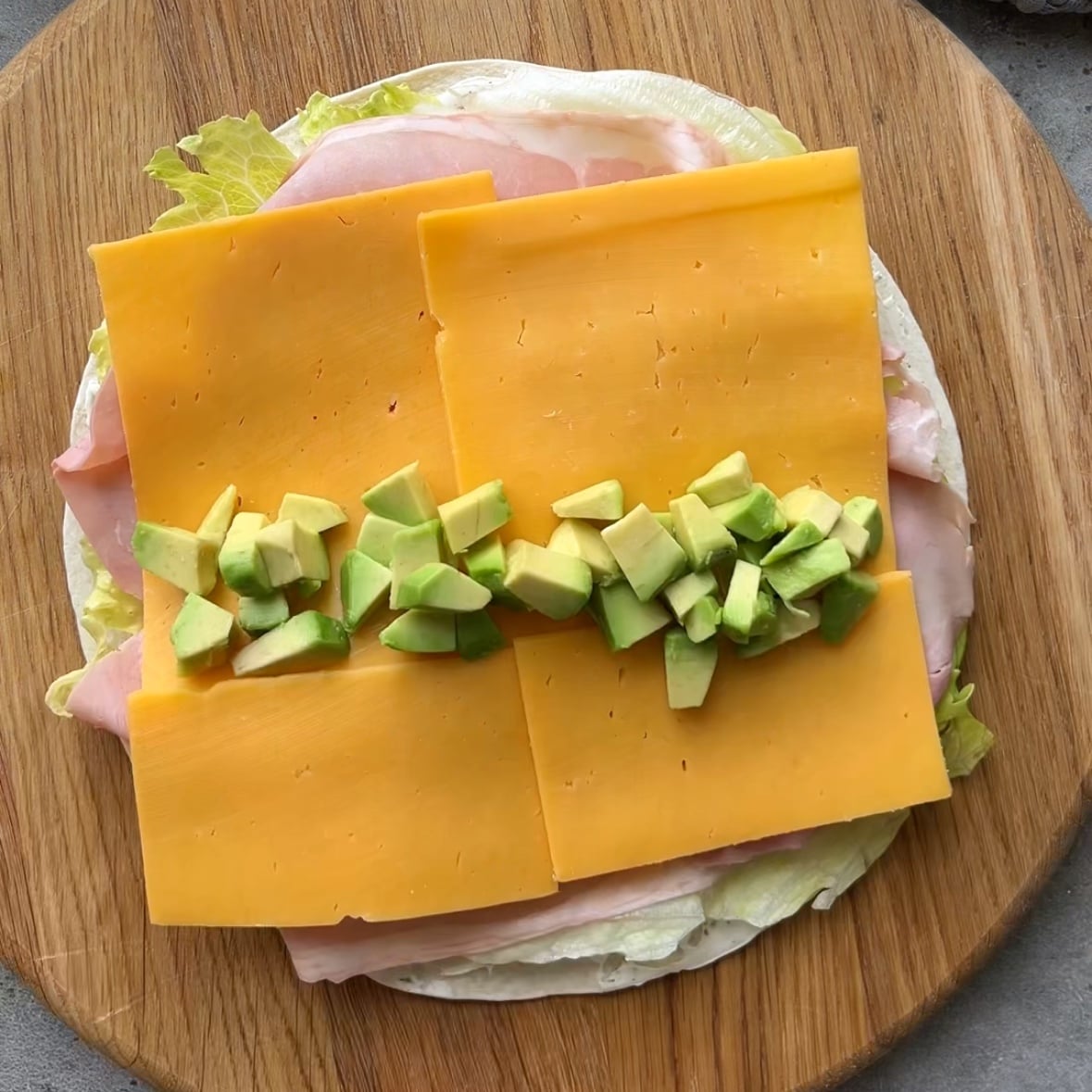 A tortilla topped with cream cheese, iceberg, ham, cheddar, and avocado.