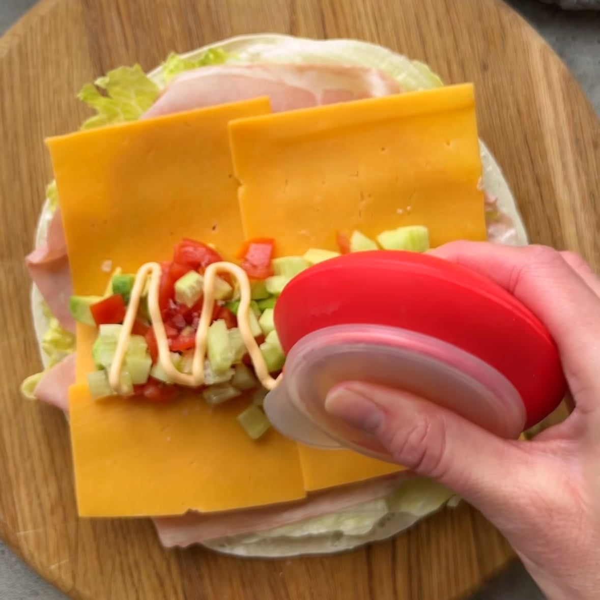 A piping utensil is topping a salad wrap with chili aioli.