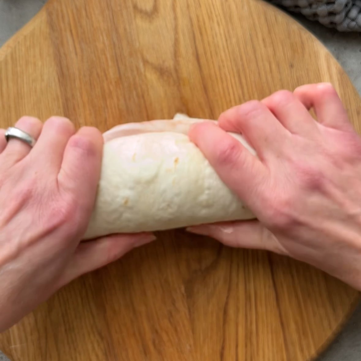 Two hands are rolling up a salad wrap tightly.