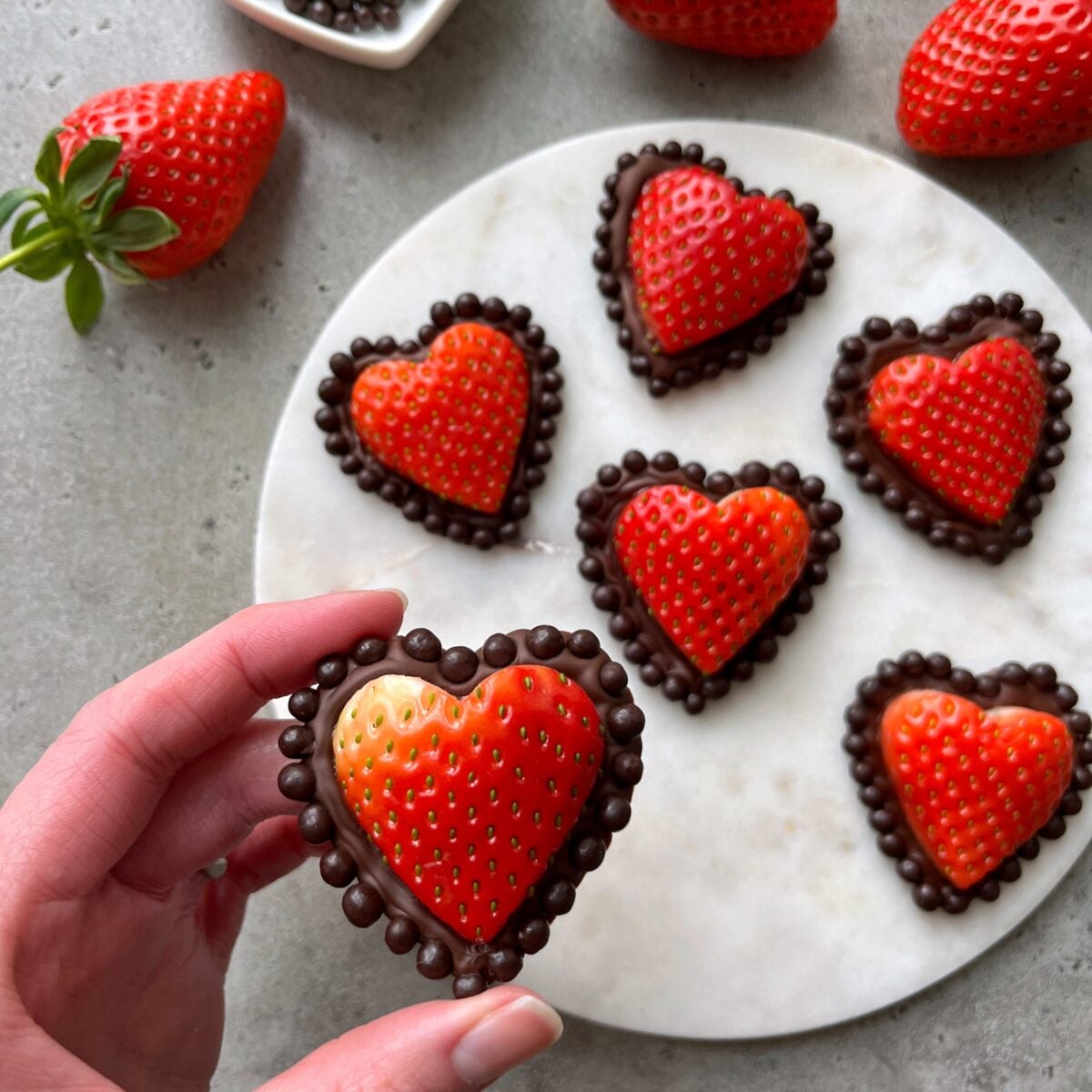 A hand holds a Strawberry Chocolate Heart with a chocolate dot border.