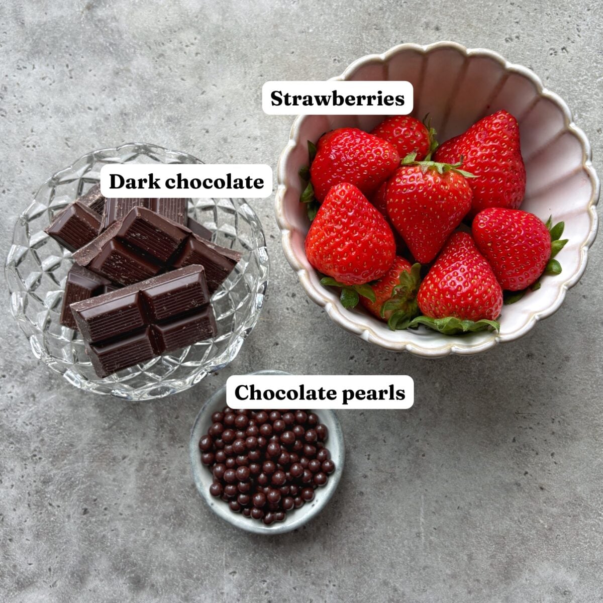 A bowl of strawberries, a dish of dark chocolate pieces, and a small bowl of chocolate pearls.