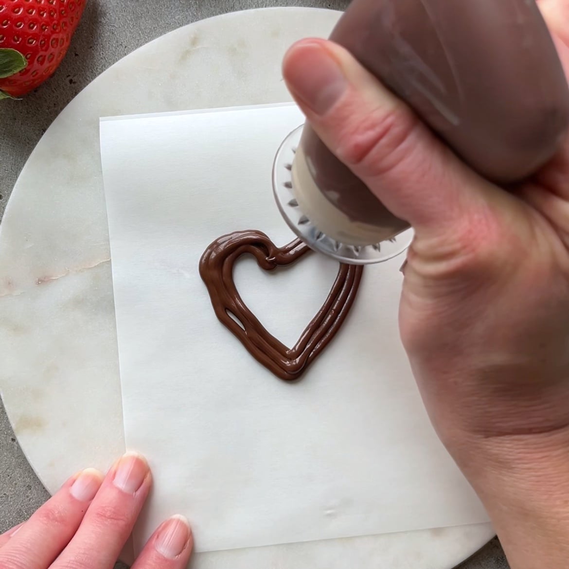 A hand pipes a dark chocolate heart.