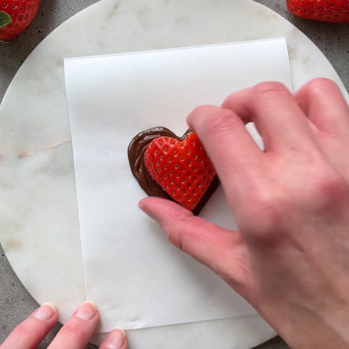 A hand places a strawberry heart on top of a dark chocolate heart.