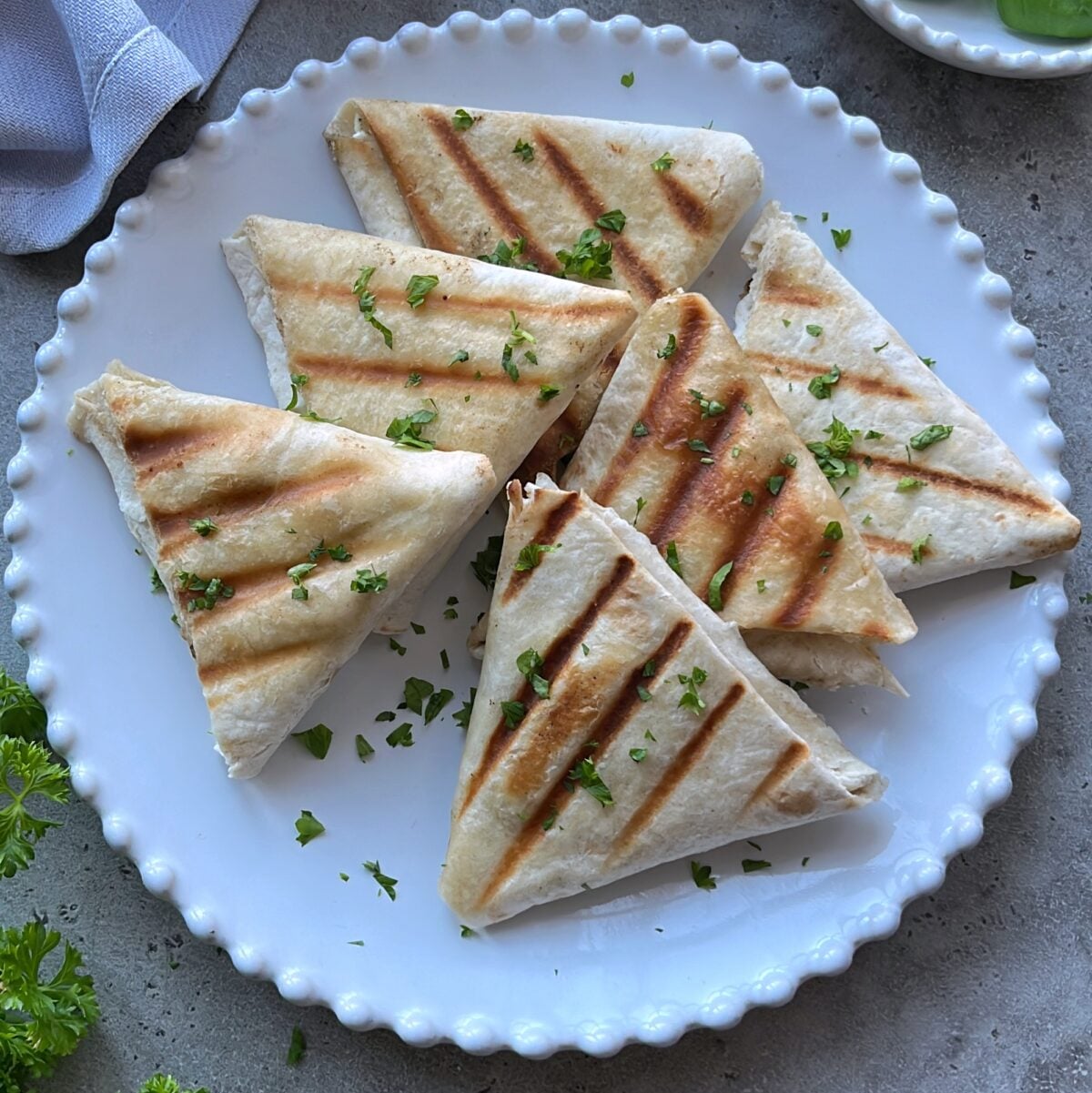 Grilled tortilla triangles arranged on a white plate, garnished with chopped parsley.