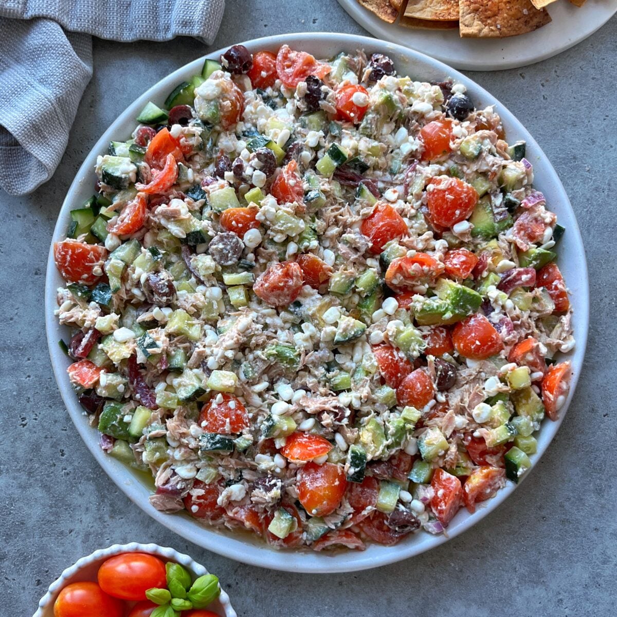 A large plate of Tuna Cottage Cheese Salad with cherry tomatoes, cucumbers, red onions, feta cheese, olives, and chunks of tuna mixed with dressing.