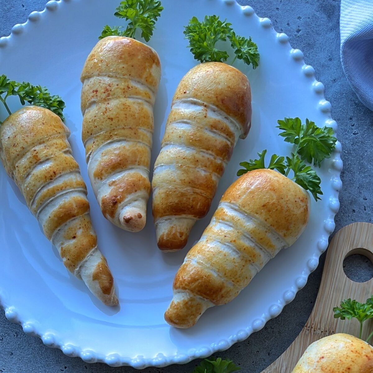 Four easter rolls shaped like carrots with parsley tops, are arranged on a white plate.