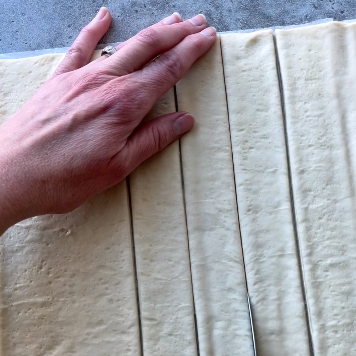 A hand rests on sheeted dough cut into long, even strips on a gray countertop.