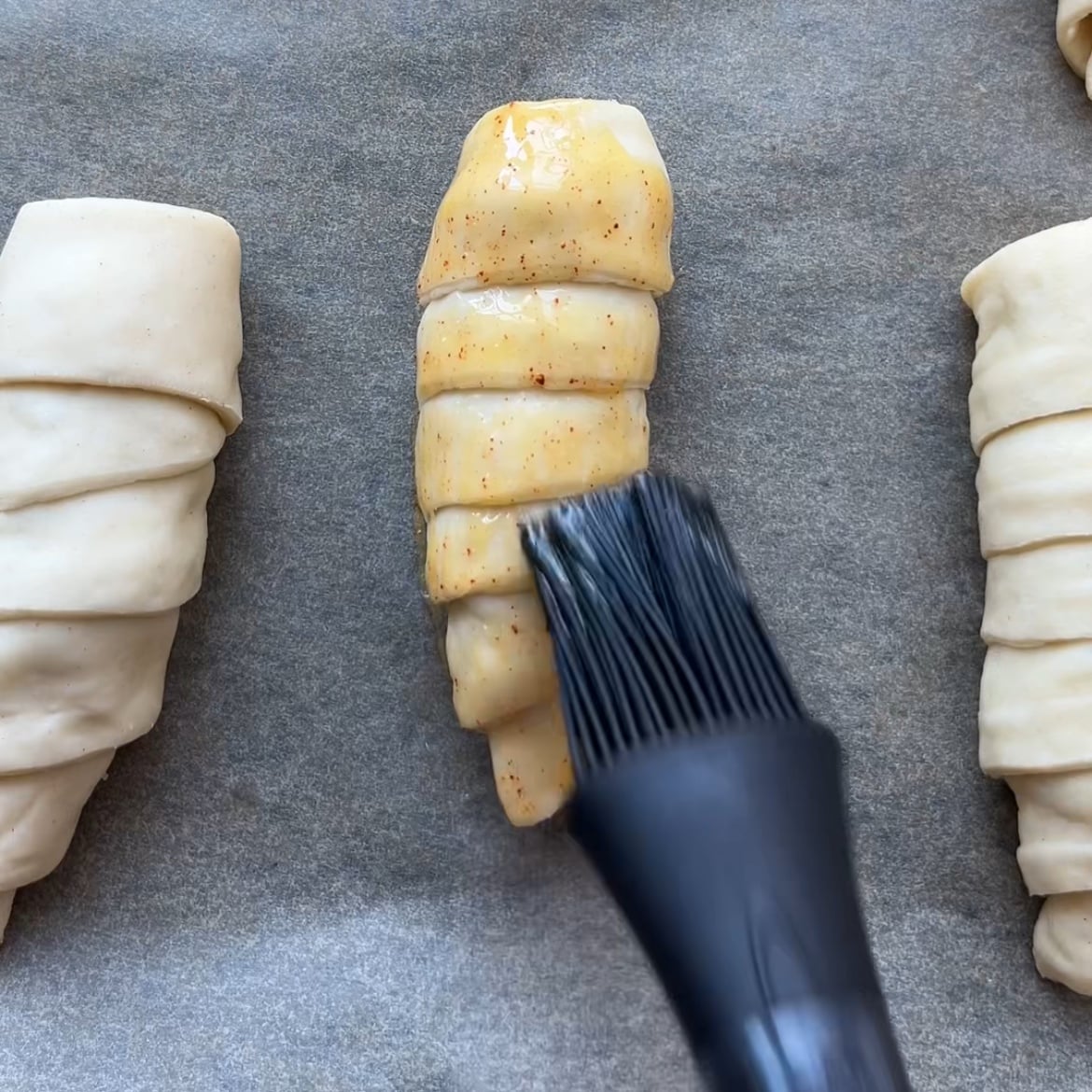 A silicone brush applies egg wash to an unbaked, rolled pastry.