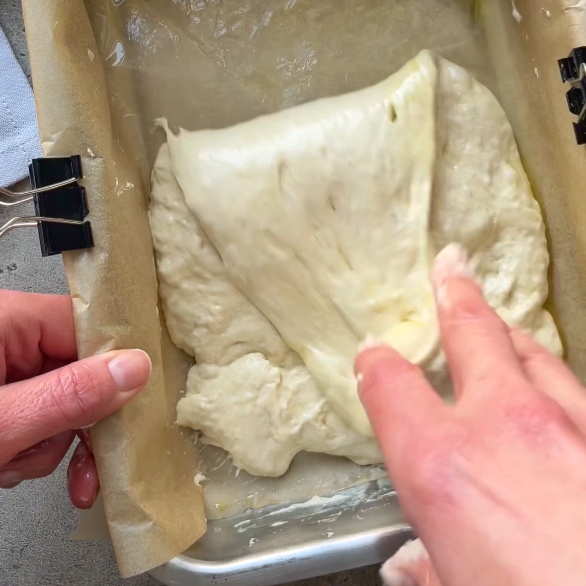 A hand stretches and folds focaccia dough. 