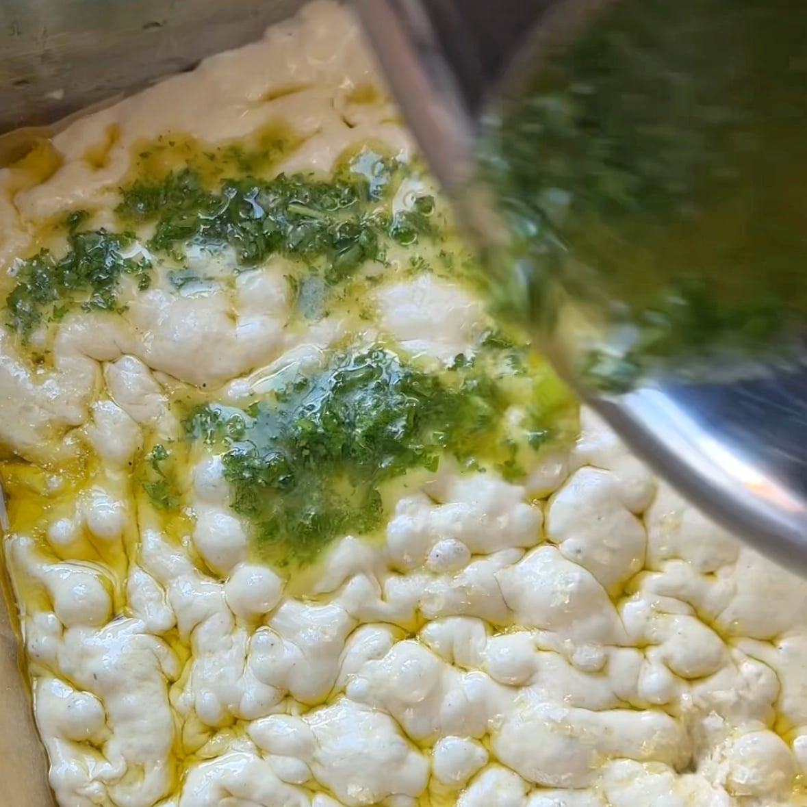 Garlic butter is being poured on top of a dimpled focaccia dough.