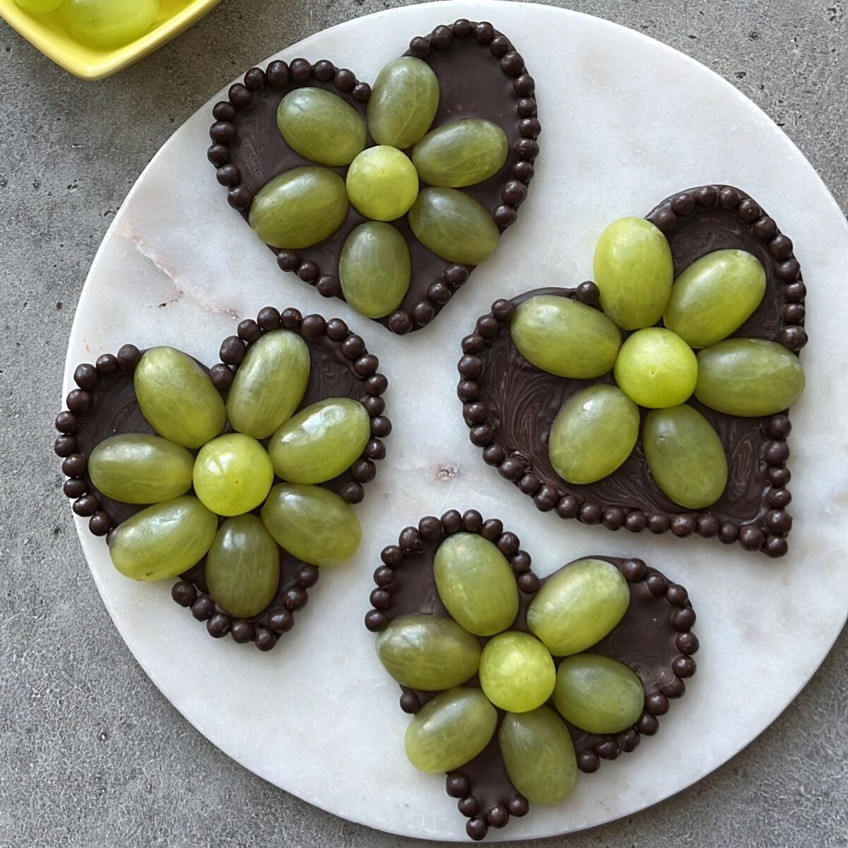 Four Grape Chocolate Hearts are decorated with green grapes arranged like flowers with small chocolate balls along the edges.