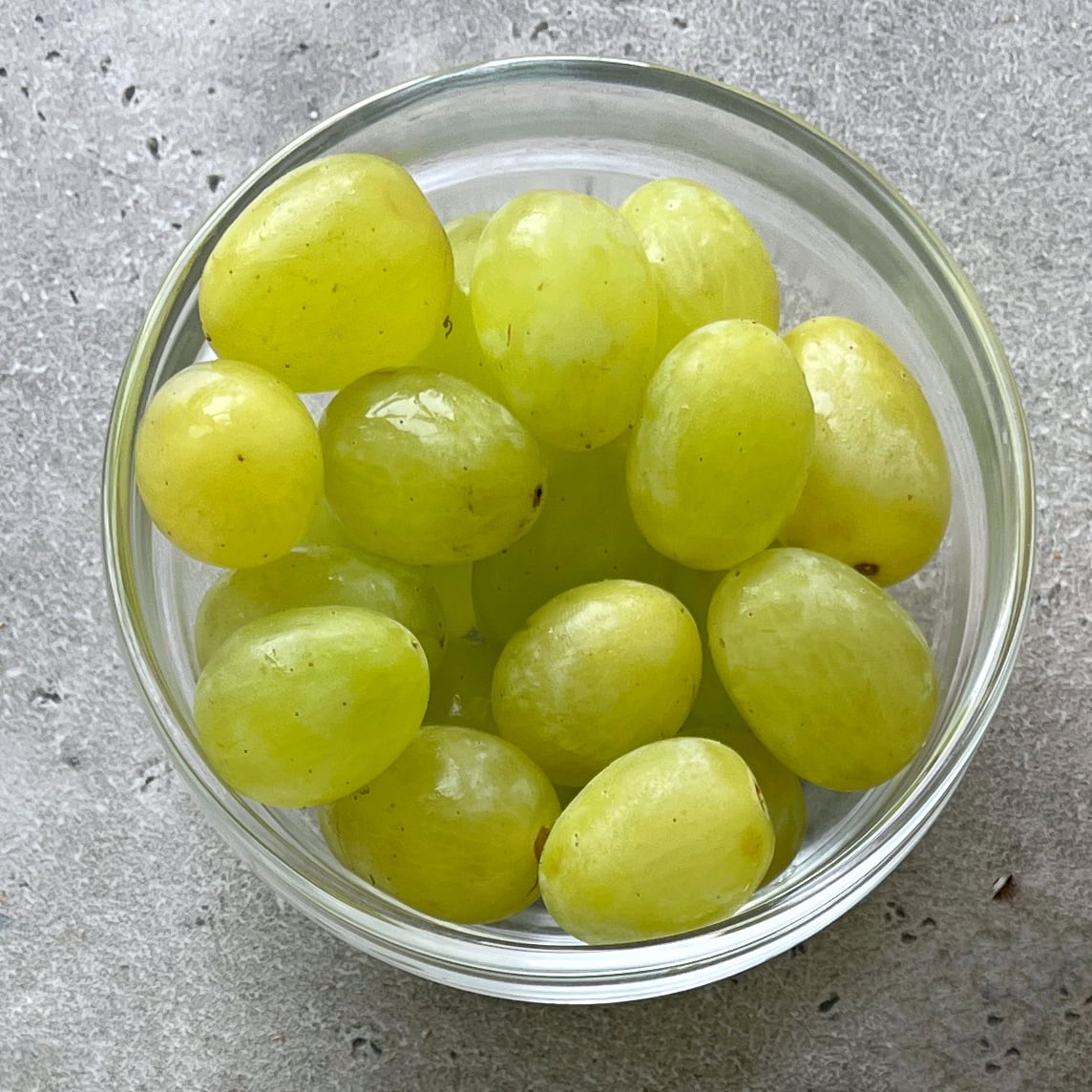 A glass bowl filled with green grapes.