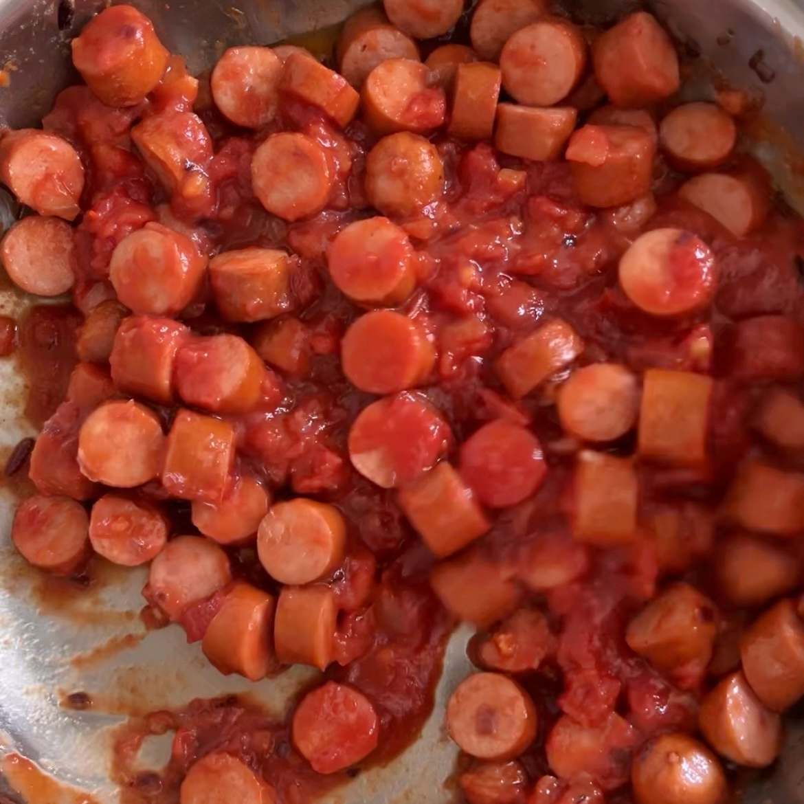 Sliced sausage pieces mixed with tomato sauce in a pan.