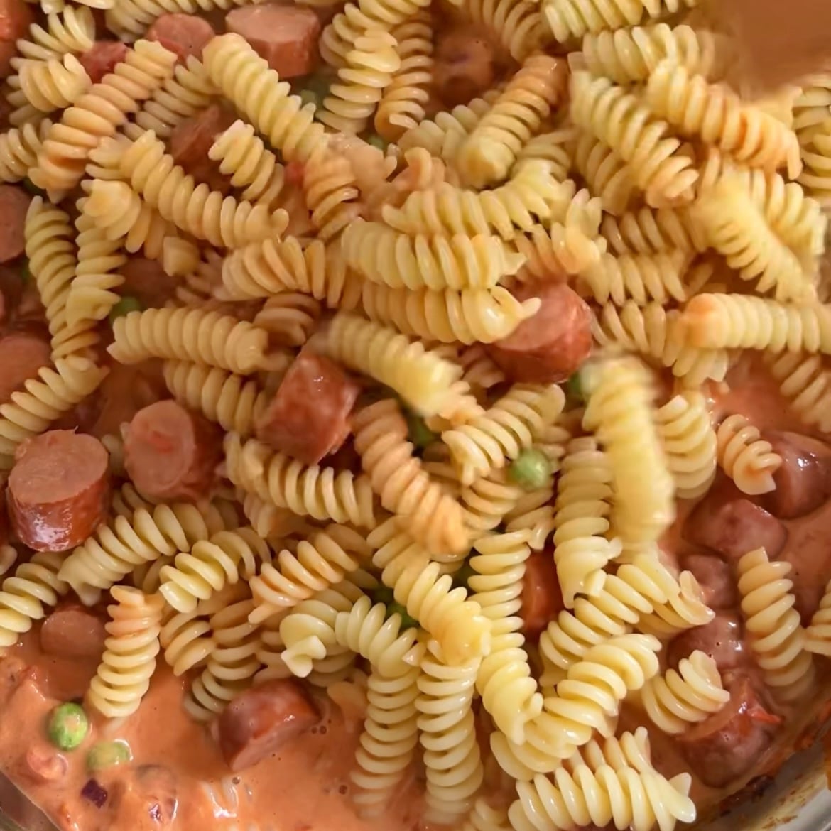 Close-up of Sausage Pasta featuring pasta mixed with sliced sausages, green peas, and a creamy tomato-based sauce.