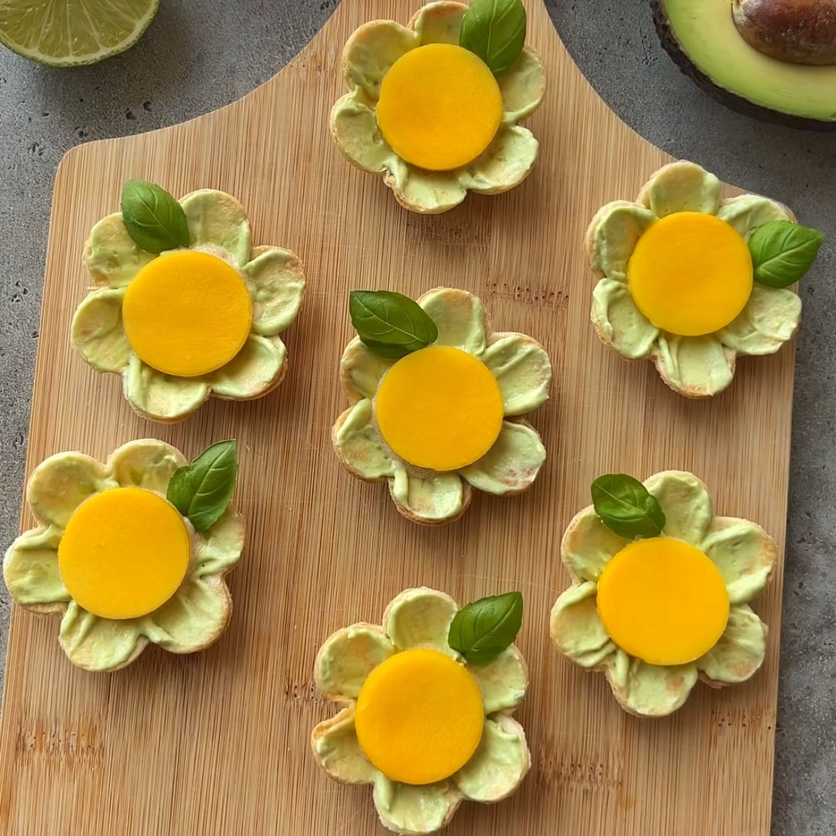 Seven flower-shaped snacks with mango centers and green leaves are arranged on a wooden board.