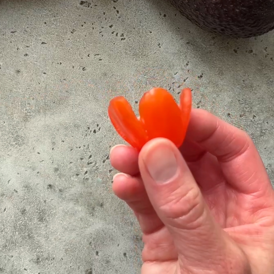 A hand holds a grape tomato shaped into a flower, ready to fill with halved bocconcini.