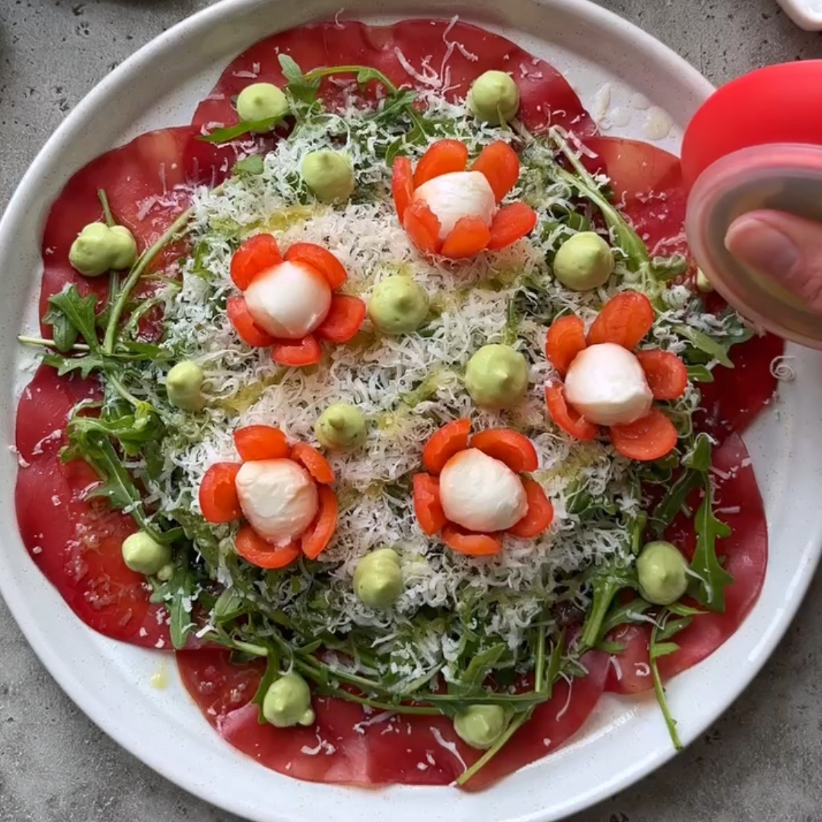 A hand dollops avocado dressing onto a beef carpaccio salad platter as the finishing touches.