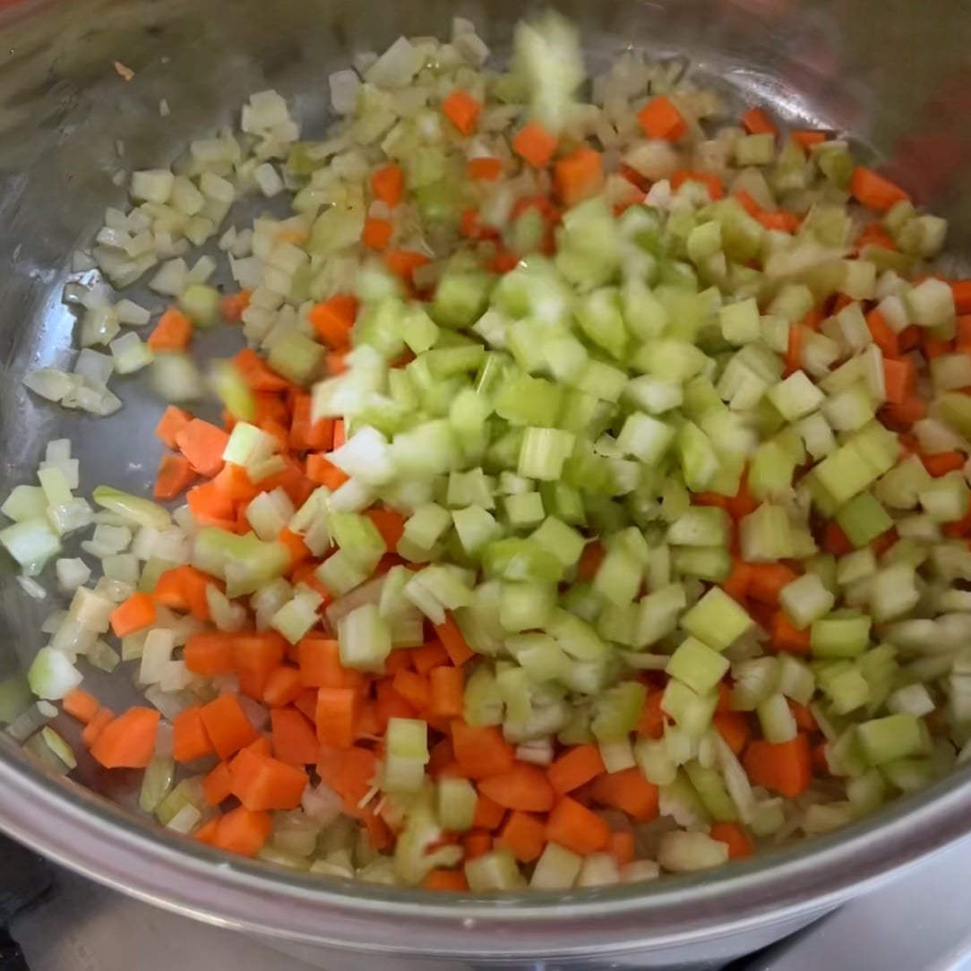 Diced onions, carrots, and celery sizzle in a metal pan.
