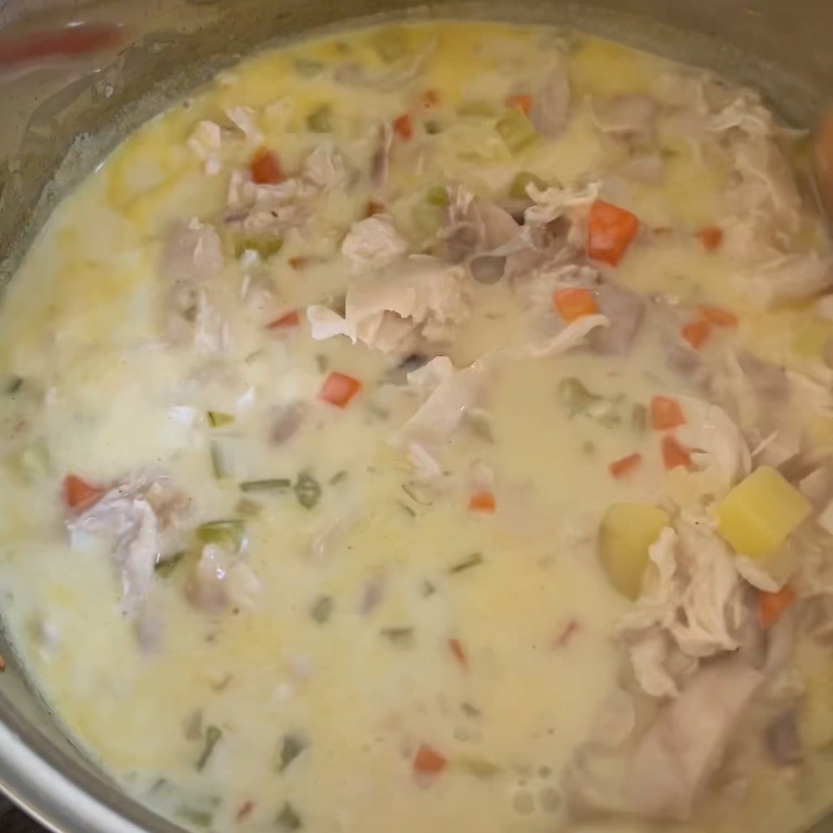 Close-up of a pot of creamy Chicken Potato Soup, featuring tender chicken, carrots, potatoes, and celery.