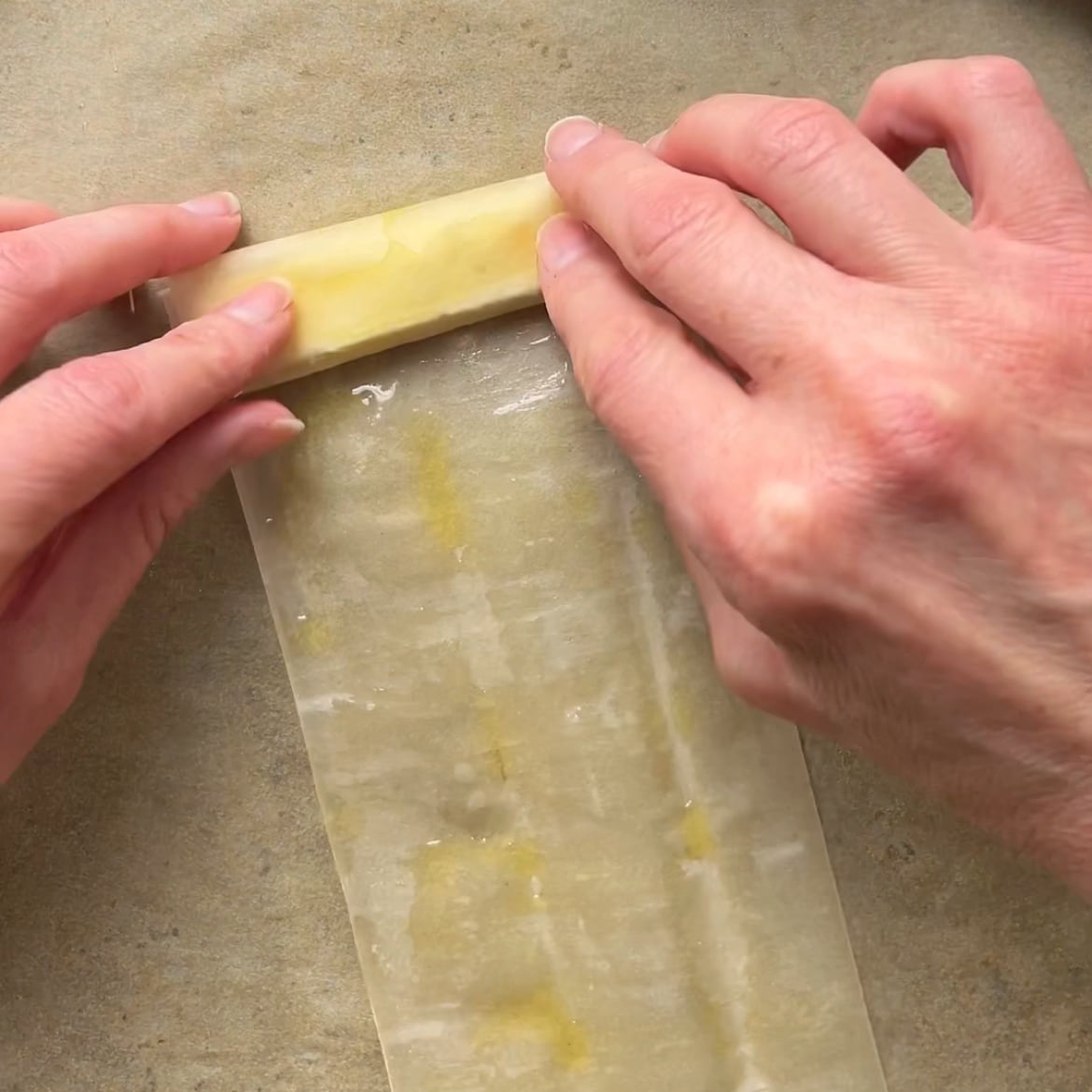Two hands are rolling a feta slice into a phyllo sheet.