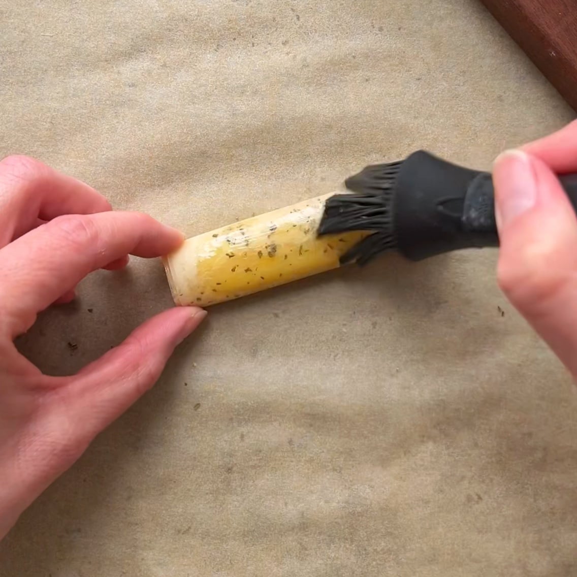 A person uses a silicone brush to apply olive oil onto a phyllo feta fry.