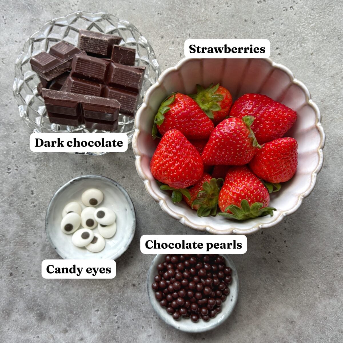 Four bowls contain dark chocolate pieces, whole strawberries, candy eyes, and round chocolate pearls, all labeled with text.