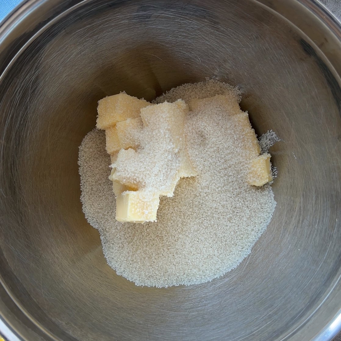 A stainless steel mixing bowl containing cubed butter and granulated sugar, ready to create the perfect Fruit Pizza base.