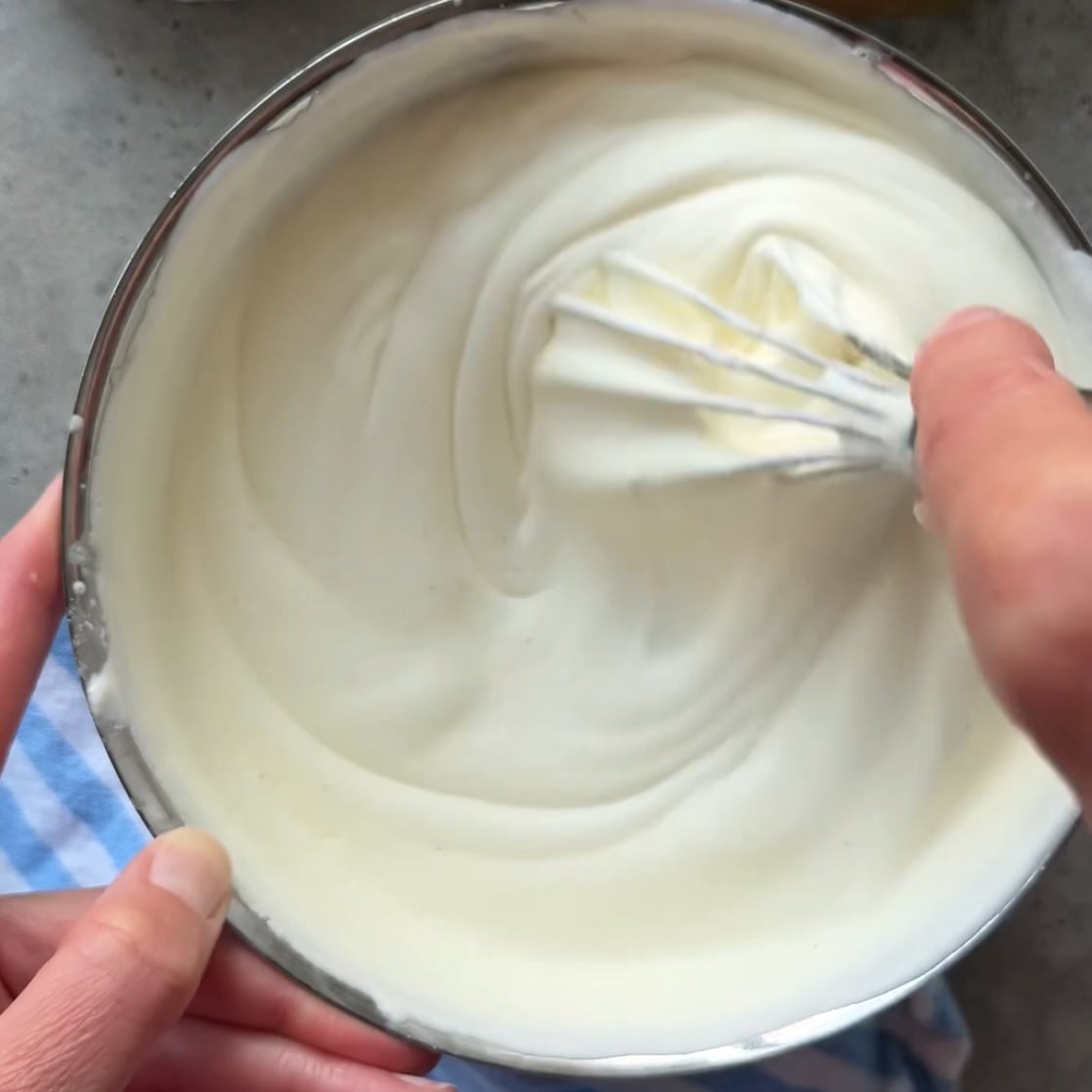 A person whisking thick, white mascarpone cream in a metal bowl.