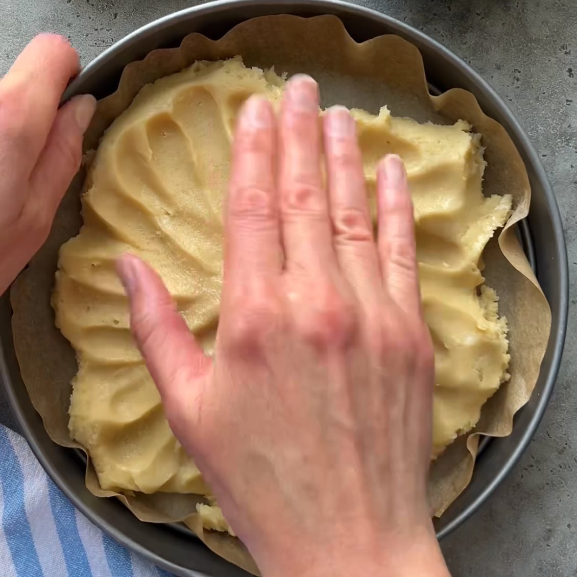 A person presses dough evenly into a parchment-lined round baking pan preparing the base for a delicious Fruit Pizza.