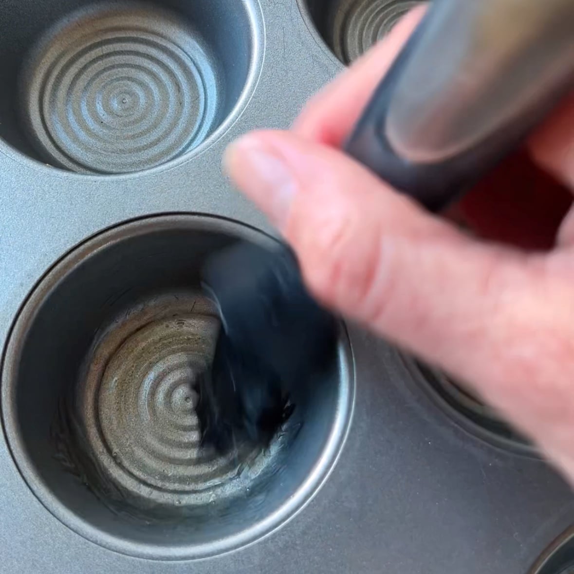 Hand brushing melted butter onto a muffin tin cup to prepare it for baking delicious Mashed Potato Cups.