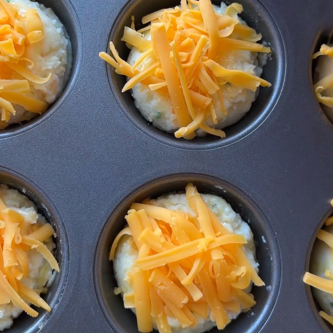 Muffin tin filled with unbaked Mashed Potato Cups, topped with shredded cheddar cheese, ready to be baked.