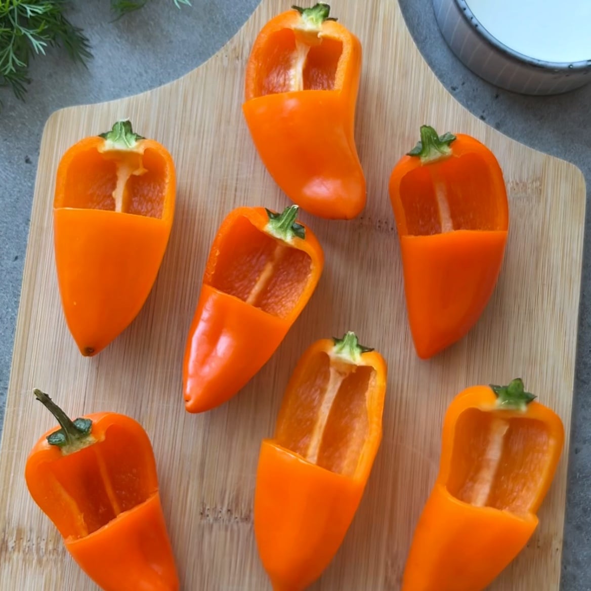 Seven orange bell peppers with cut outs are arranged on a wooden cutting board.