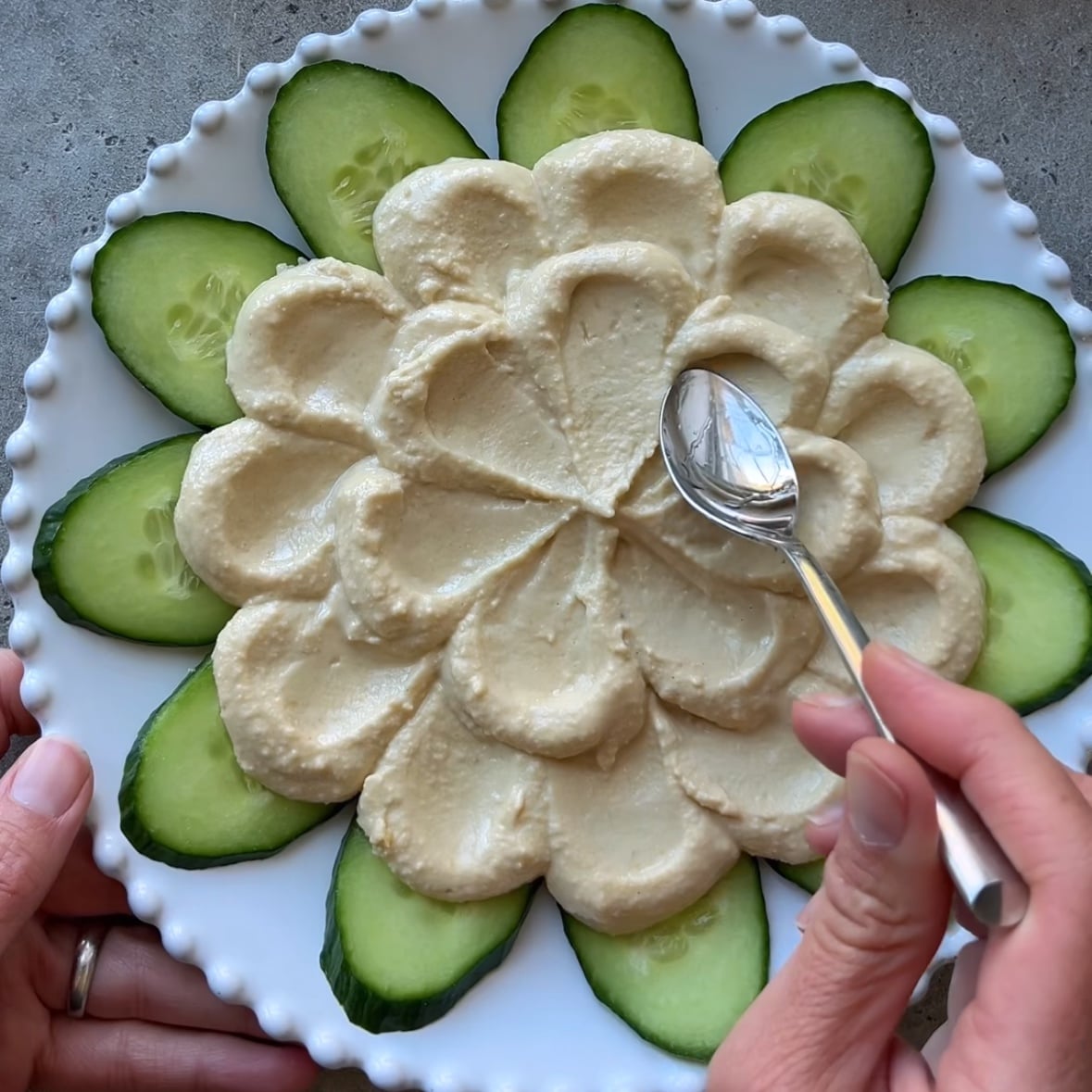 A wet spoon smooths hummus arranged in petals.