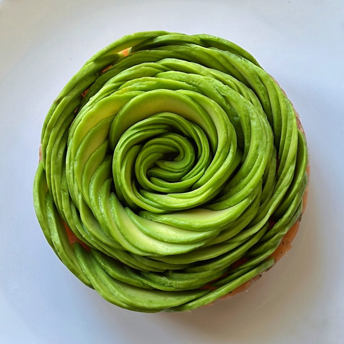 Smoked salmon tartare topped with thinly sliced avocado arranged in a spiral rose pattern on a white plate.