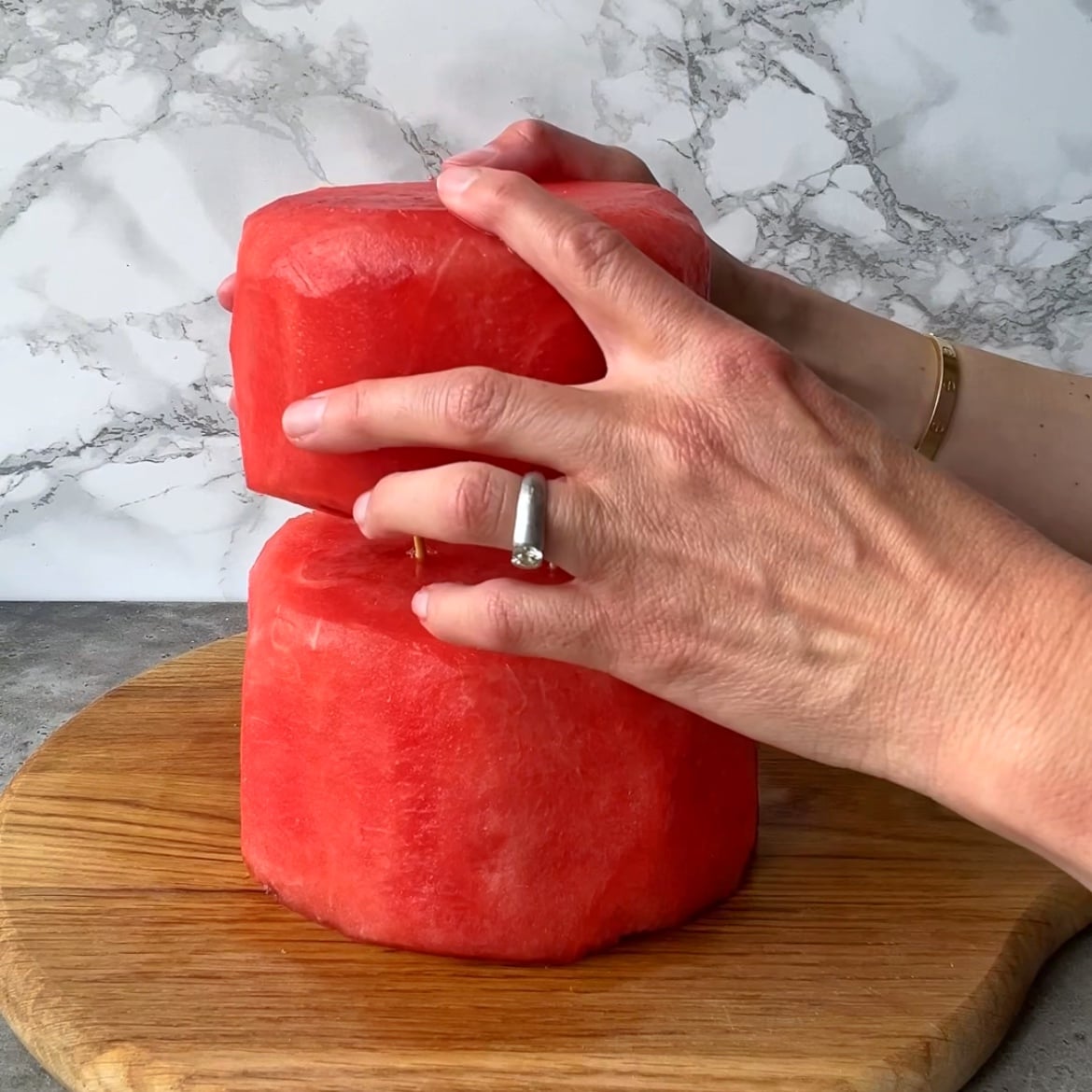 Two hands stack one watermelon on top of another to make a Watermelon Fruit Cake.