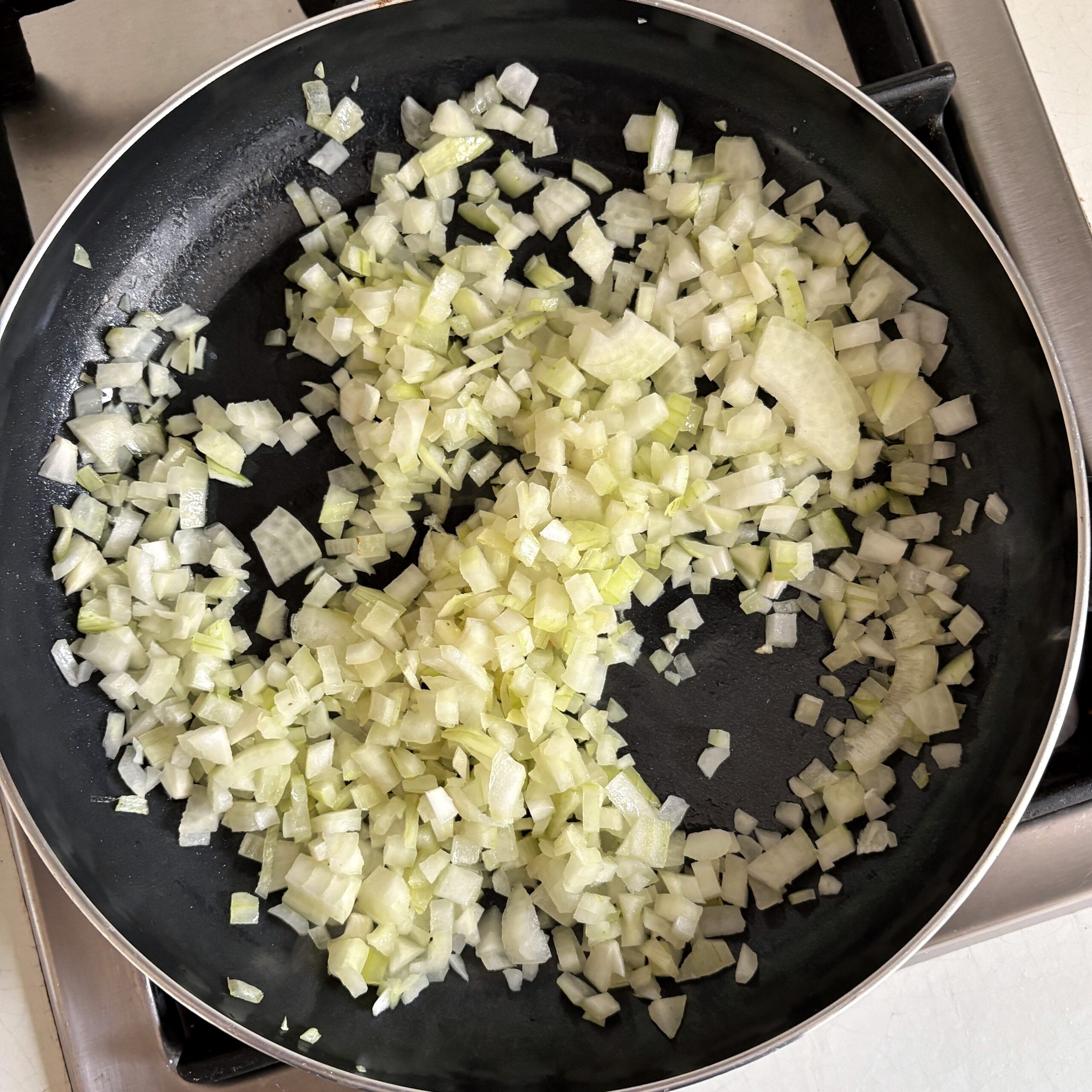 Chopped onions are being sautéed in a black frying pan on a stove.